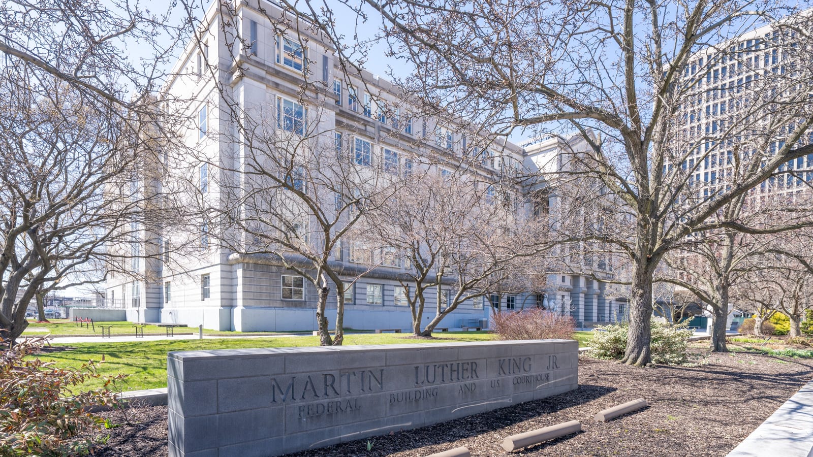 The stone Martin Luther King Building and U.S. Courthouse in Newark behind bare trees, with its name carved on a low granite wall.